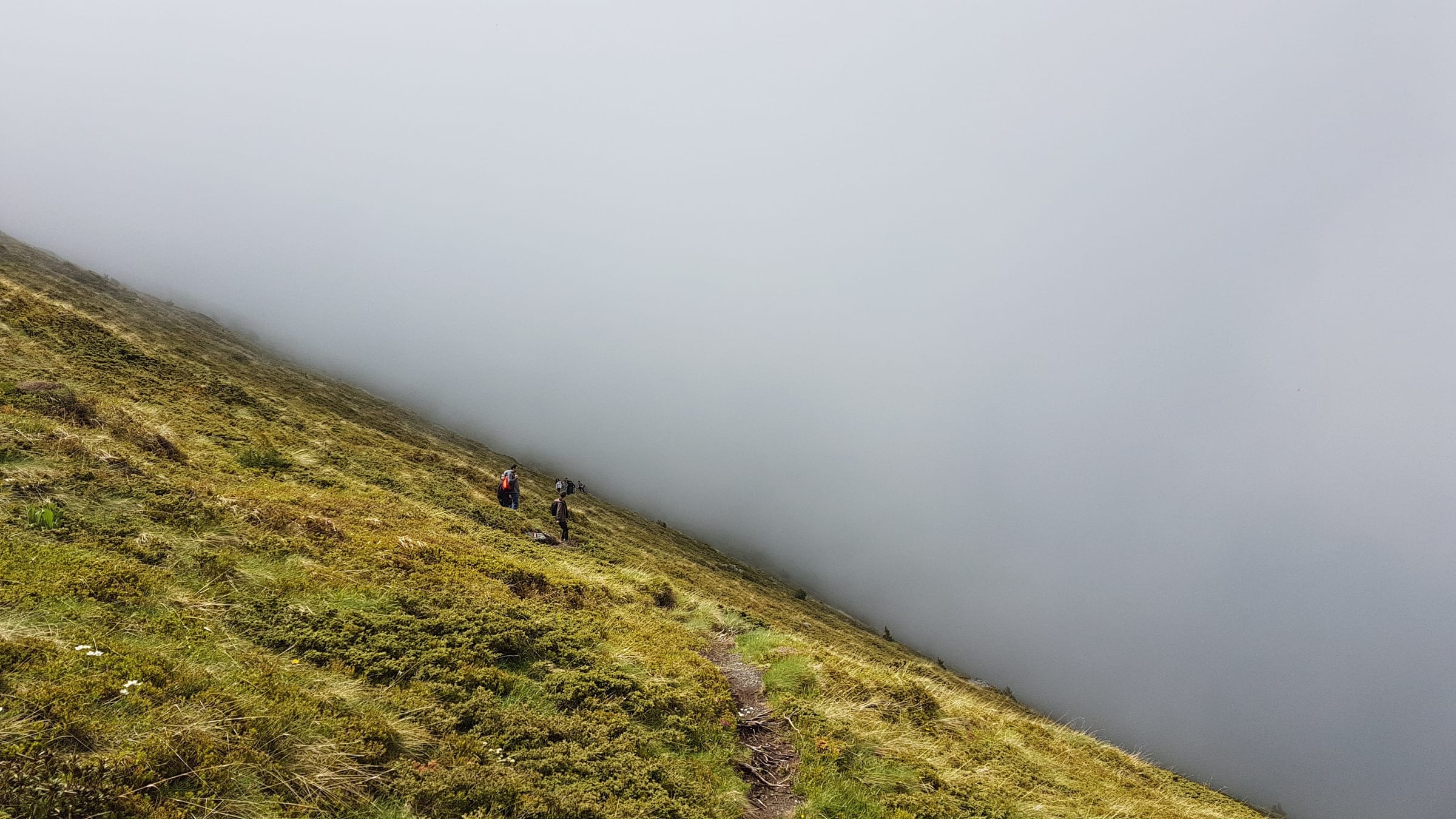 Dos senderistas en una ladera herbosa de Mali i Livadhit, en Oshlak, mientras la niebla engulle el valle a su lado