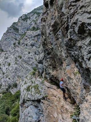 A climber in a red helmet on a ledge of the Rugova Canyon via ferrata beneath the gorge wall