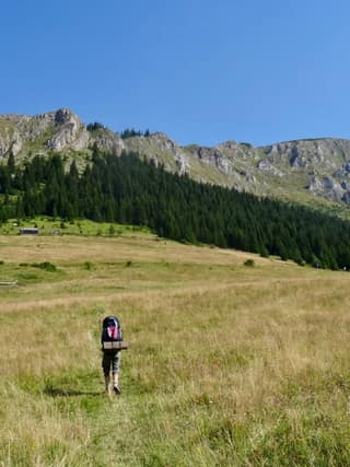 A hiker with a backpack, back to the camera, crossing the meadow on the south side of Hajla in the Rugova mountains