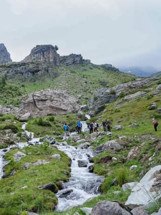 A line of hikers beside the stream that tumbles from the cliffs below Gjeravica in the Deçan mountains