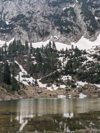 Liqenat in spring, its still water mirroring the pines and snow patches of the cirque walls above