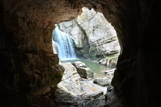 The main Mirusha waterfall framed by the dark mouth of the cave beside its pool