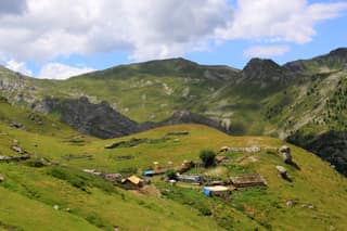 The summer huts of the Pllaqica katun on a green shelf below the peaks between Gjeravica and the Tropoja mountains
