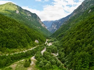 The Rugova gorge from the air in summer, the road and the pale riverbed winding between forested walls