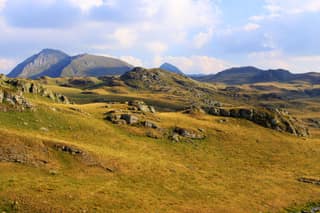 Golden late-summer grass and limestone outcrops on the Shutman plateau above Brod, with the Sharr peaks behind
