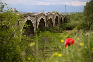 The stone arches of Ura e Terzive, the eighteenth-century Tailors' Bridge near Gjakova, behind a poppy in the spring grass