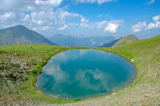 The round glacial lake of Tropoja on the border pastures above Junik, with the peaks of Bjeshkët e Nemuna behind
