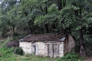 An old stone watermill with a plank door under the trees beside a stream in Dragash