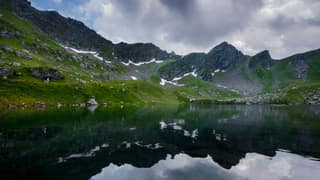 Storm clouds mirrored in Liqeni i Zemrës, the Heart Lake, beneath the cirque of the Deçan mountains